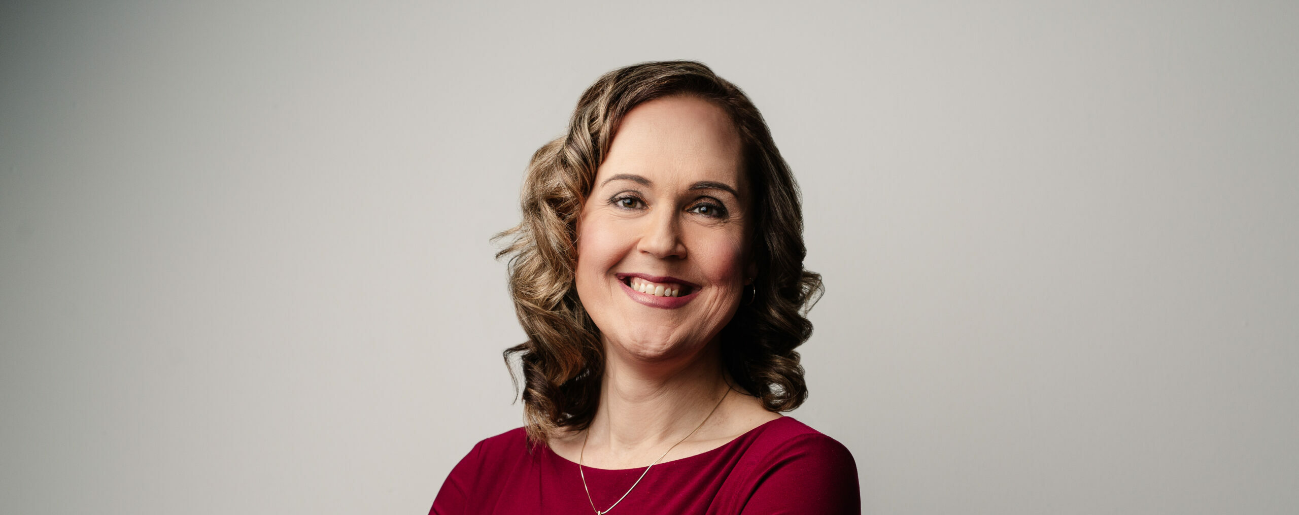 Headshot of Marni Panas. A woman with short blond curly hair wearing a black and red top smiling at the camera.