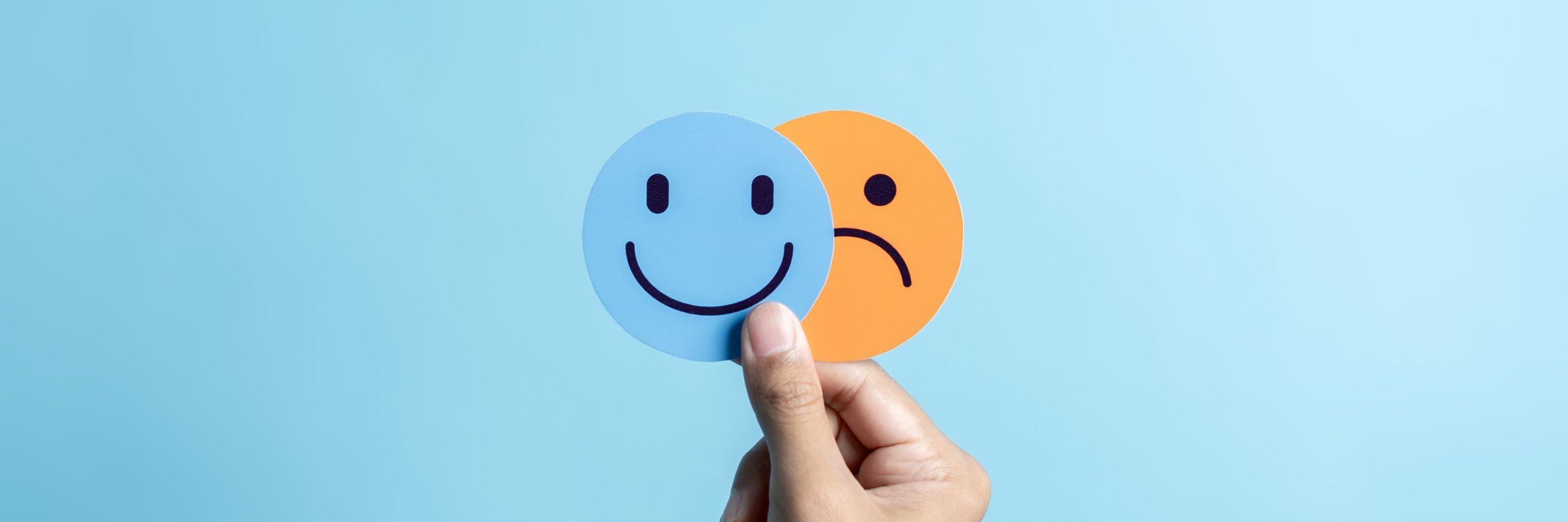 A hand holding up two pictures, one of a face smiling and one of a face frowning.