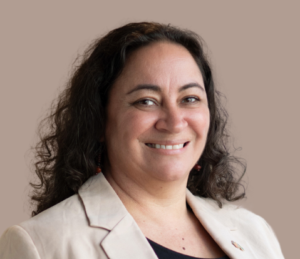 Image of Katie, wearing a cream blazer, has long curly brown hair and is smiling at the camera