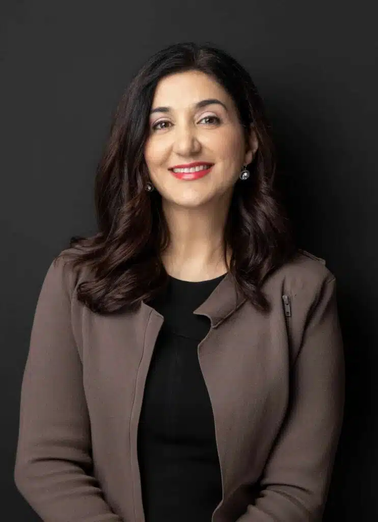 Lisa Annese in a brown and grey suit, in front of a dark grey background.